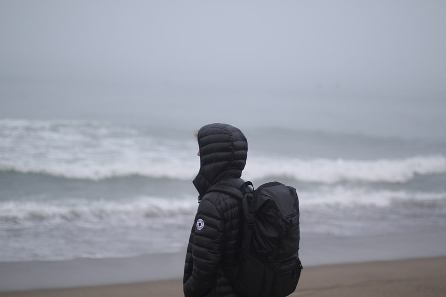 Man in black jacket looking at foggy ocean waves