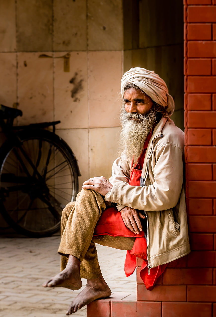 Portrait of elderly Indian man with turban sitting on brick wall
