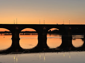 Silhouette of arched bridge over calm water at sunset