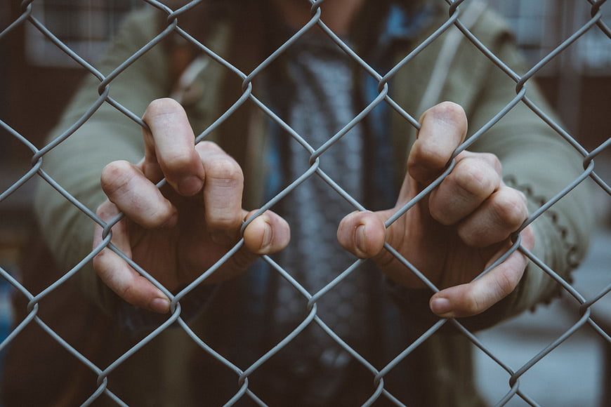 Close-up of hands gripping a chain-link fence tightly