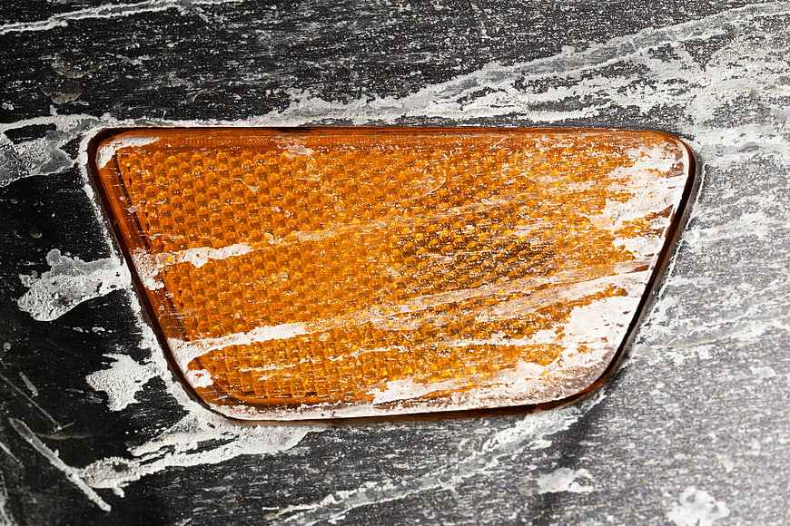 Close-up of orange car blinker covered in winter road salt