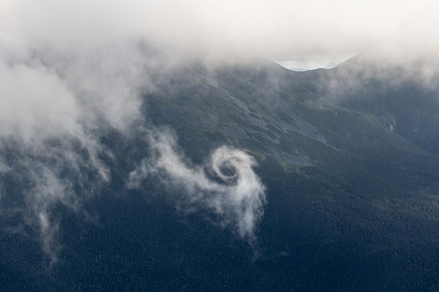 Aerial view of swirling cloud vortex over misty mountain forest