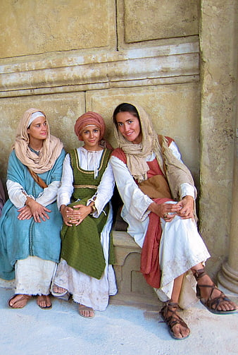 Three Women in Biblical Era Costumes Seated Against Stone Wall