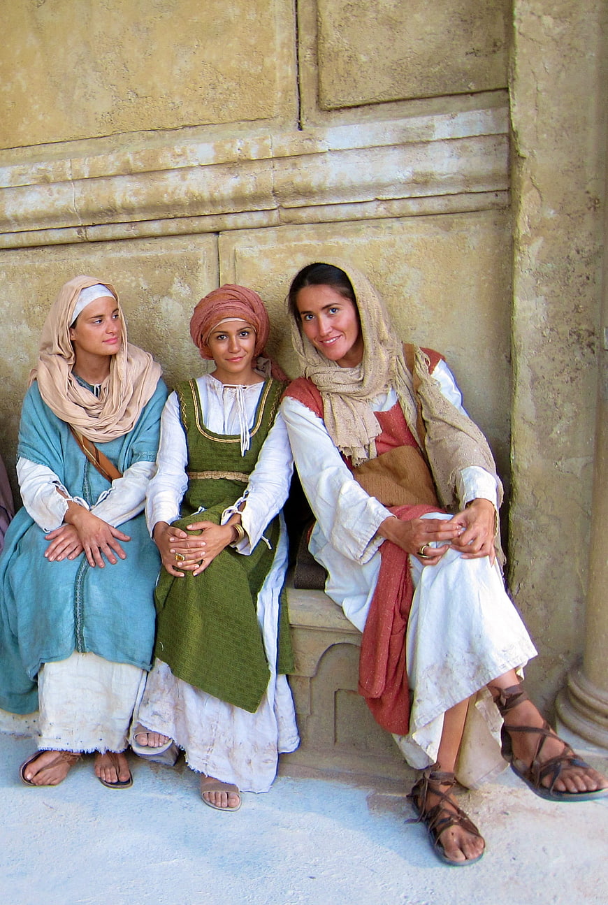 Three Women in Biblical Era Costumes Seated Against Stone Wall
