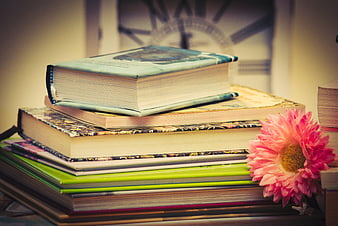 Stack of vintage books with pink flower and clock background