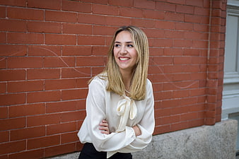 Smiling blonde woman in white blouse against red brick wall