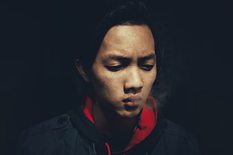 Moody portrait of a young man exhaling smoke in low light