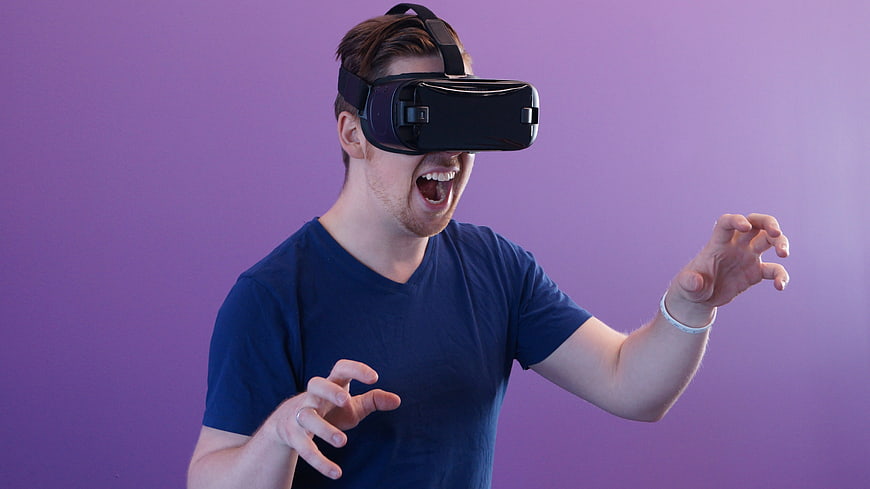 Man Wearing VR Headset Reaching Out Against Purple Background
