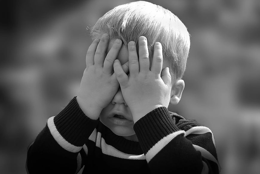 Sad young boy covering face with hands in black and white