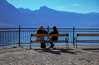 Two women chatting on a bench by a lake with mountains