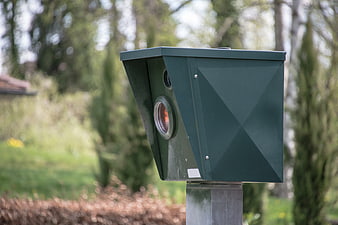 Green speed camera on a post in a park setting