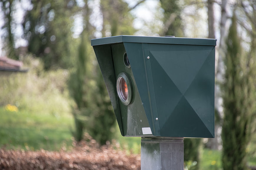 Green speed camera on a post in a park setting