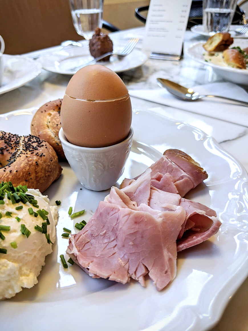 Soft boiled egg with ham, bread, and chive butter on white plate