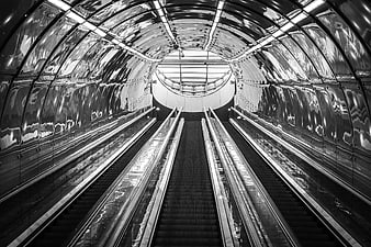 Symmetrical black and white escalators in a reflective tunnel