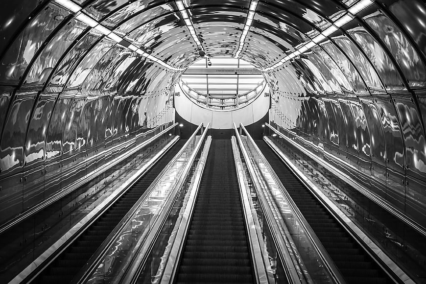 Symmetrical black and white escalators in a reflective tunnel