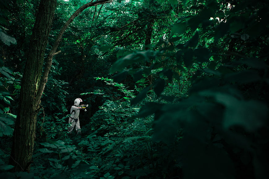 Person in white hazmat suit exploring dense green forest