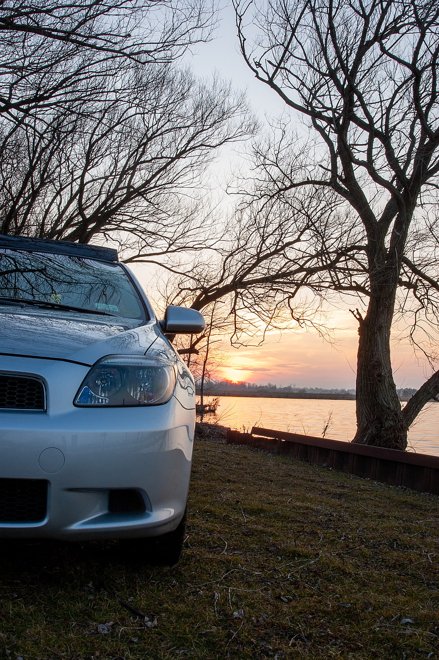 Silver Car Parked by Lake at Sunset with Bare Trees