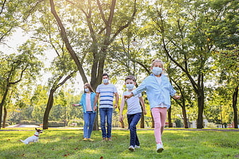 Happy family with dog walking in park wearing face masks