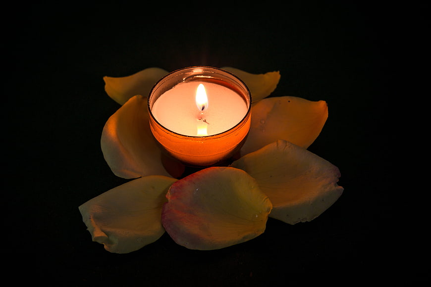 Lit Tea Light Candle Surrounded by Rose Petals on Black Background