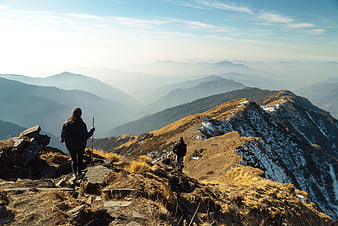 Hikers on Mountain Ridge with Snowy Peaks and Blue Sky