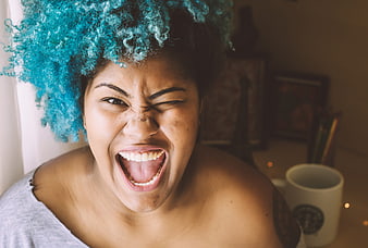 Woman with blue curly hair laughing and winking