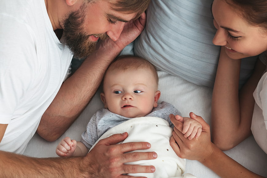 Top View of Parents Lying in Bed with Newborn Baby