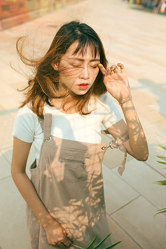 Young woman in overalls with windblown hair in sunlight