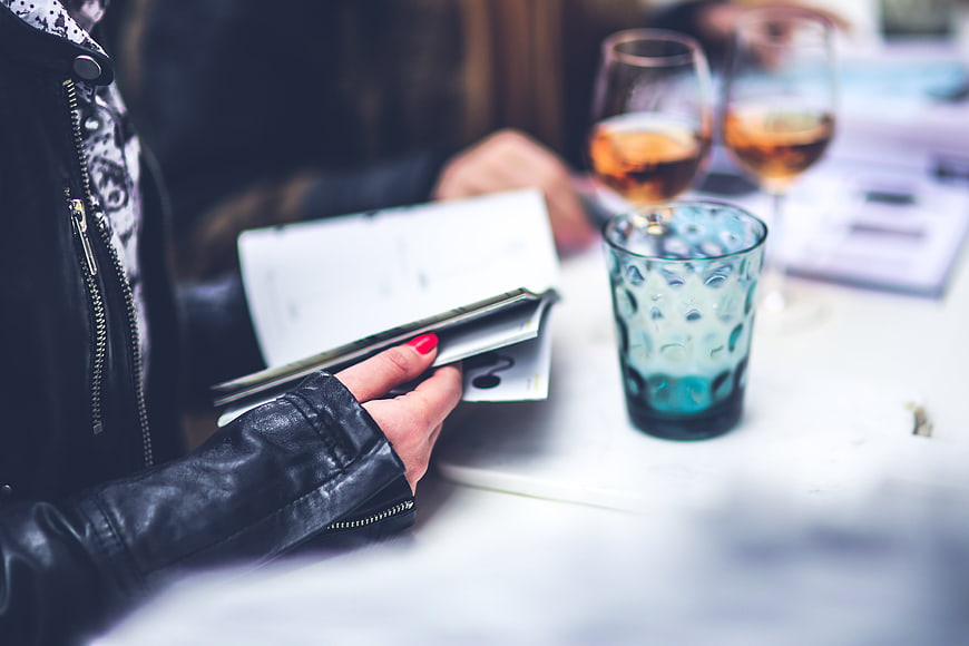 Woman in black leather jacket reading a menu at a cafe table