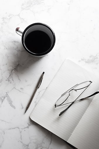Minimalist workspace with coffee, notebook, and glasses on marble