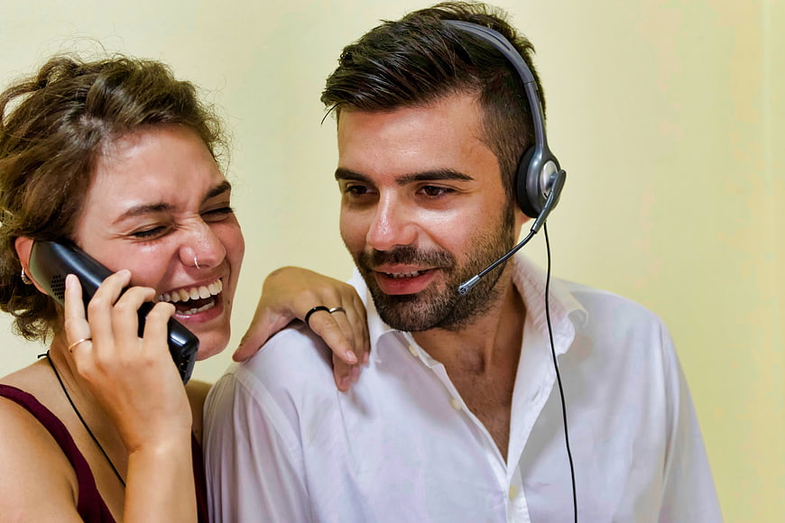 Happy couple laughing with phone and headset in office