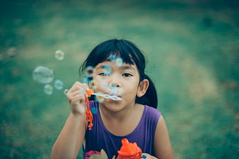 Young Girl Blowing Bubbles Outdoors in Purple Shirt