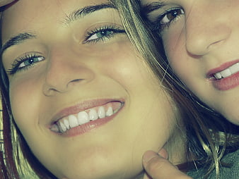 Close-up selfie of two smiling young women with warm lighting