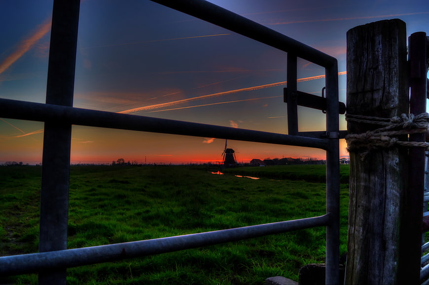 Dutch windmill silhouette at sunset through metal gate