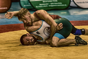 Two male wrestlers grappling intensely on a yellow competition mat