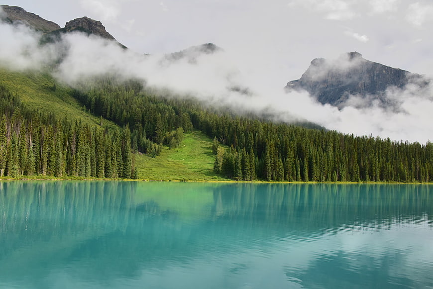 Misty turquoise mountain lake with pine forest reflection