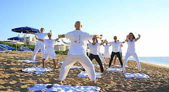 Group Tai Chi Practice On A Sunny Beach With Blue Umbrellas