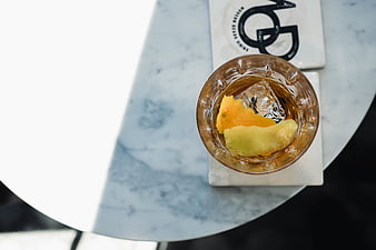 Top view of whiskey cocktail with orange peel on marble table