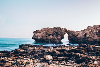 Natural Rock Arch on Rocky Coastline with Blue Ocean