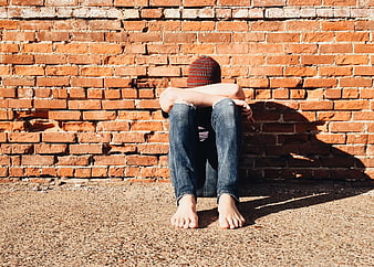 Young Person Sitting Alone Against Red Brick Wall