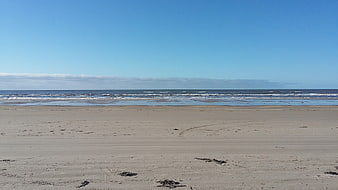 Wide sandy beach with blue sky and ocean waves