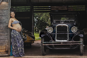 Pregnant woman posing with vintage car in rustic garage