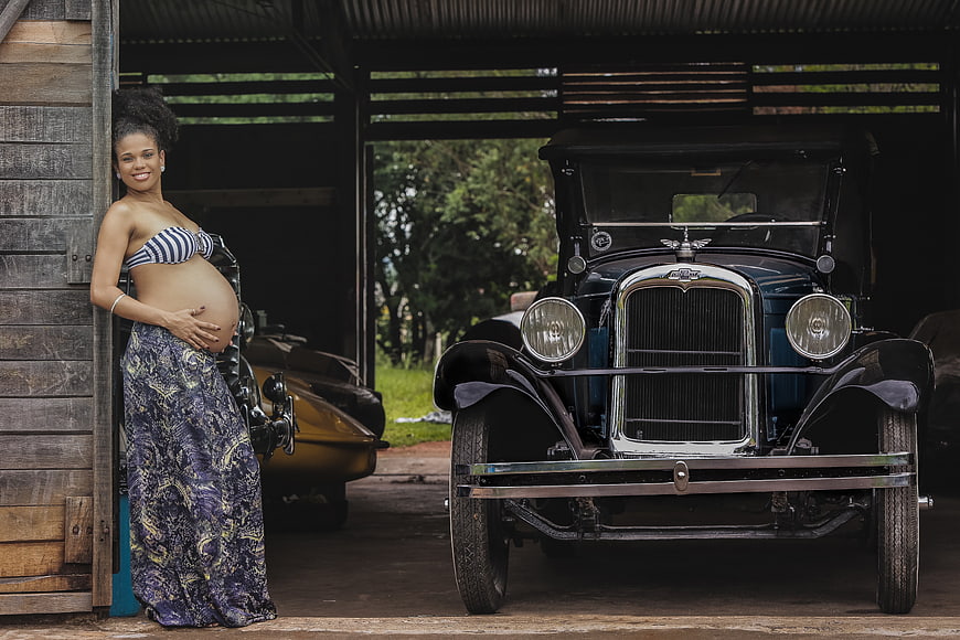 Pregnant woman posing with vintage car in rustic garage