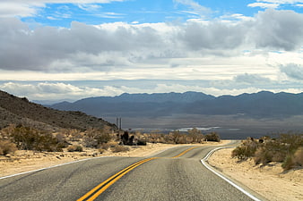 Scenic Desert Highway Leading To Distant Mountain Range Under Cloudy Sky