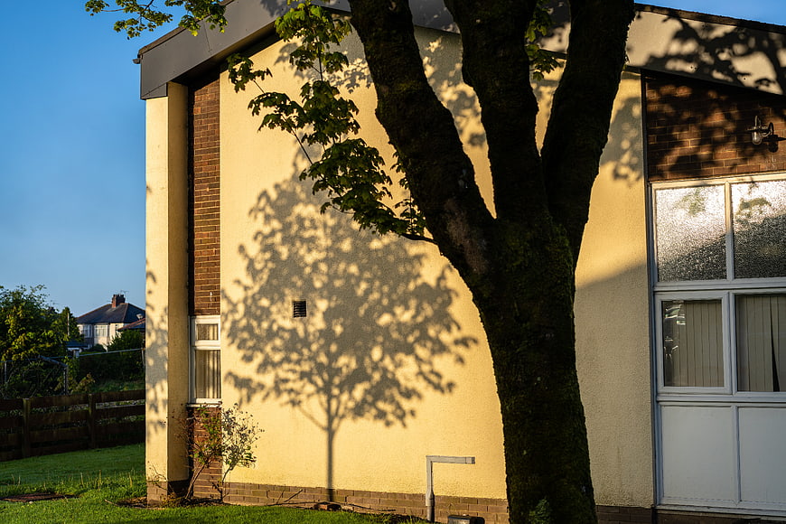 Sunlit House Exterior with Tree Shadow on Yellow Wall