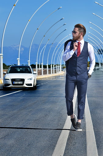 Stylish man in suit walking on road with luxury car