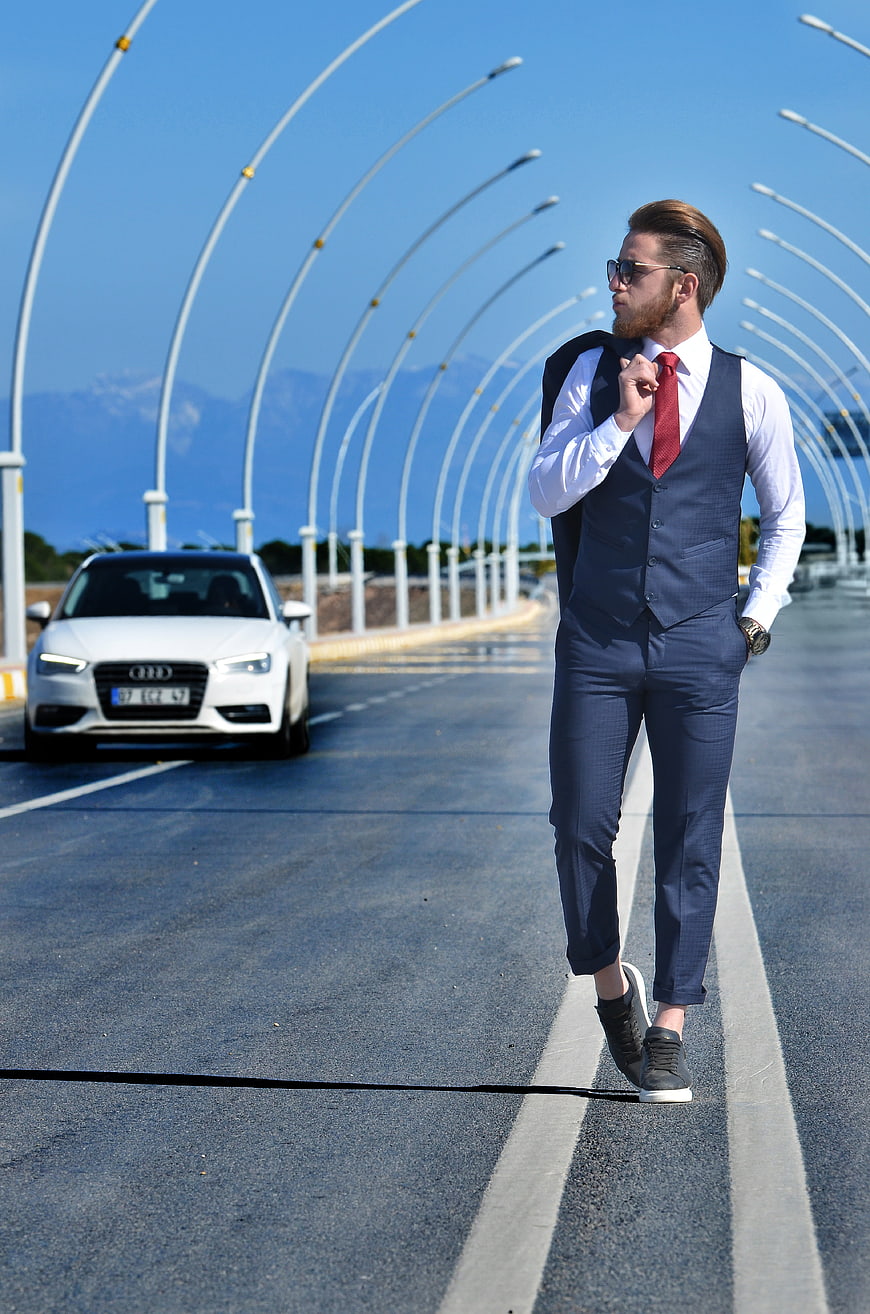 Stylish man in suit walking on road with luxury car