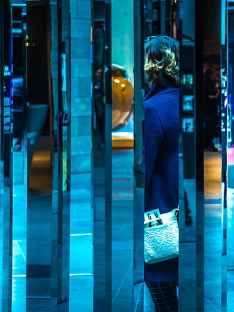 Woman with white bag seen through blue mirrored columns