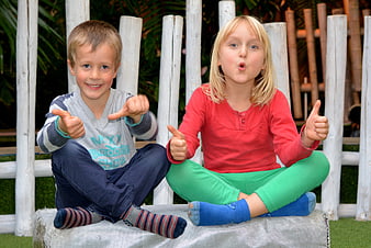 Two children giving thumbs up while sitting on a bench outdoors
