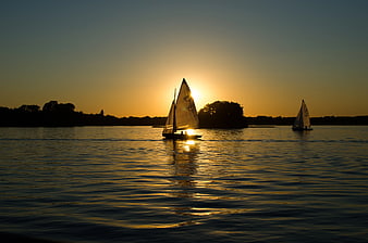Sailboats Silhouetted Against Golden Sunset on Calm Water