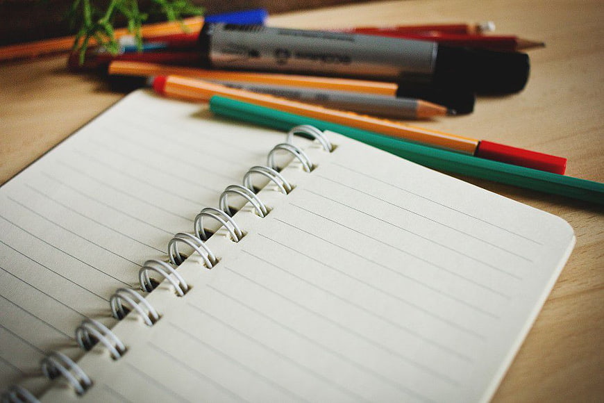 Open Spiral Notebook with Colored Pencils and Markers on Desk